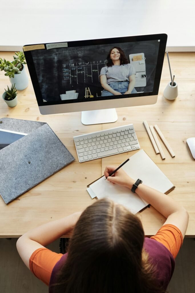 A teenage student attentively participates in a virtual classroom setting from a home office workspace.